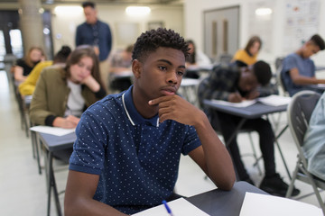 Thoughtful high school boy taking exam at desk in classroom