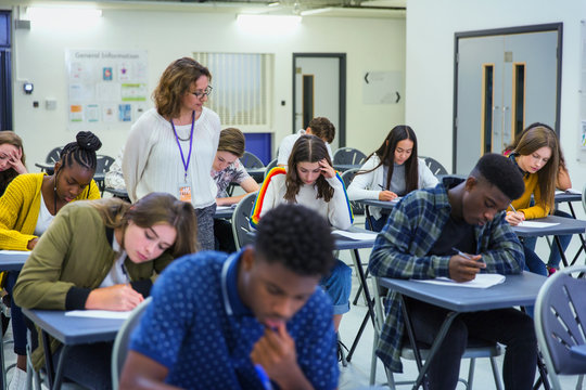 High school teacher supervising students taking exam at desks