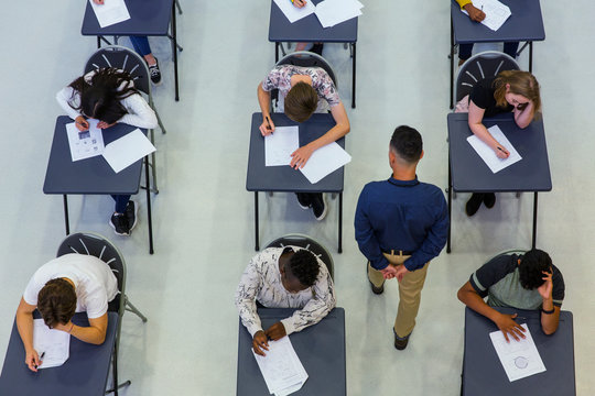 High school teacher supervising students taking exam at desks