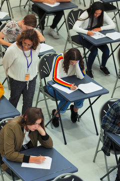 High school teacher supervising students taking exam at desks