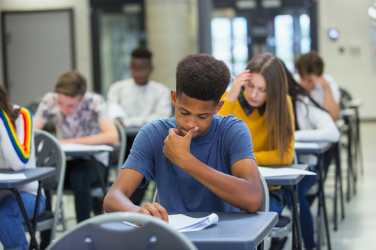 Focused high school boy student taking exam at desk in classroom
