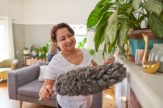 Mature woman with duster dusting living room