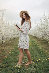 Girl reading a book in the spring garden. Gorgeous woman in hat and dress on nature. Camping with a book.