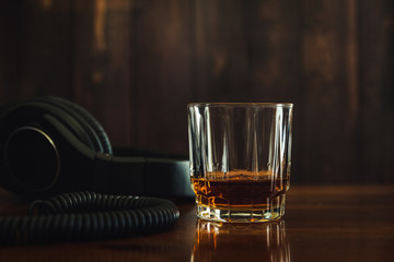 A glass of whiskey neat on the table with headphones next to the glass. 
