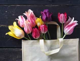Fresh Tulip flowers in a natural fabric bag on a dark wooden table.Top view with a copy of the space.