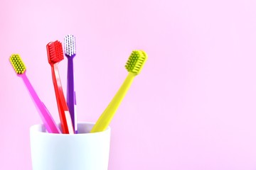 Four bright colourful soft toothbrushes with selective focus in white mug on pink neutral background. New toothbrush for dental hygiene. 