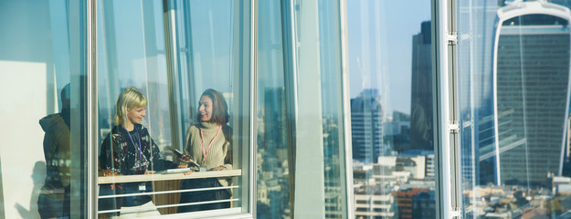 Businesswomen talking at sunny urban highrise office window