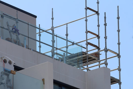 Steel scaffolding on a modern muti story apartment building. Also pictured is a glass balustrade ladder and electrical cables. Blue sky background.