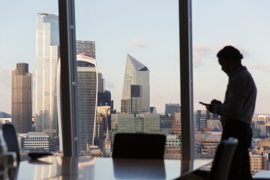 Fototapeta Silhouette businessman using smart phone at urban highrise window