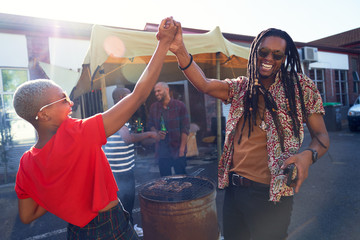 Happy friends high fiving and barbecuing in sunny parking lot