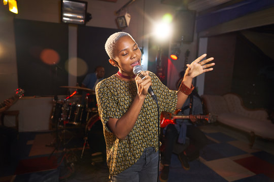 Young female musician singing into microphone in recording studio