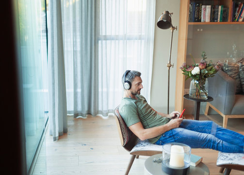 Man relaxing in living room, listening to music with mp3 player and headphones