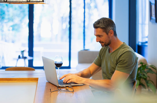 Man Using Laptop And Drinking Wine, Working From Home In Kitchen