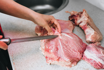A girl, a hostess, a butcher cuts with a knife raw, fresh, bloodied pork meat for cooking in the...
