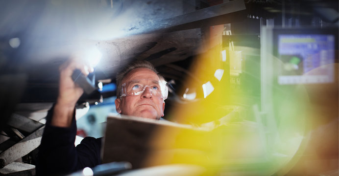 Focused male mechanic with flashlight under car in auto repair shop