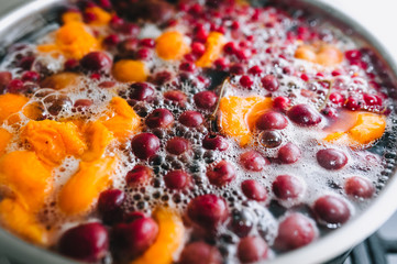 Fresh fruits: apricots, cherries, raspberries, apples are boiled in boiling water in a metal pan on a stove with bubbles and foam close-up. Cooking delicious homemade compote. Photography, concept.