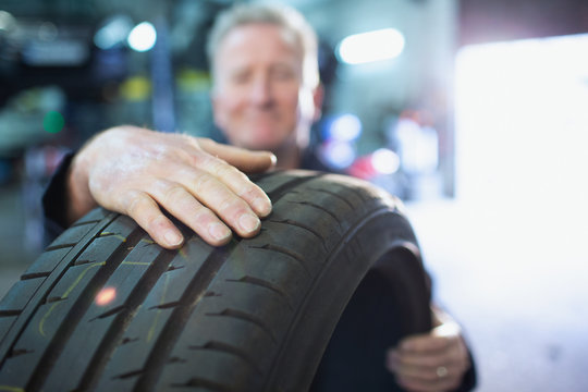 Male mechanic holding tire in auto repair shop