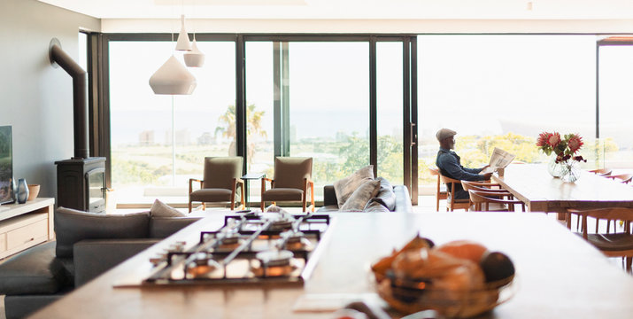 Man Reading Newspaper At Dining Table In Modern, Open Plan House