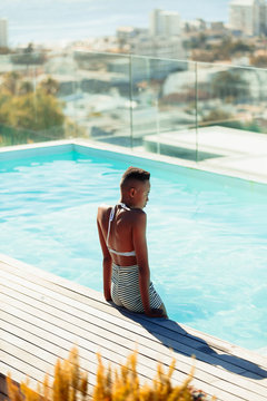 Serene young woman at sunny rooftop swimming pool