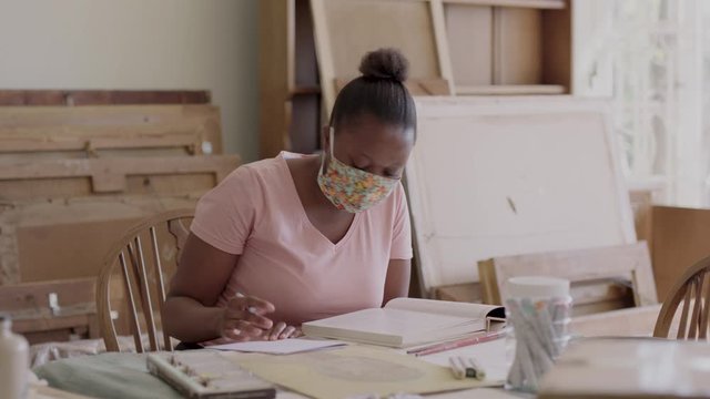 A young black woman studying while wearing a health mask.