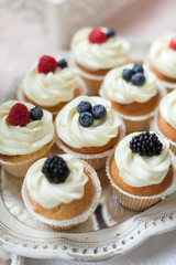 the tip of the white creamy open cake with a mix of wild berries - blueberry, raspberry, mulberry on white table