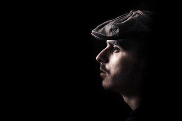 Portrait of cute young guy with moustache and a hat on black, dark background.