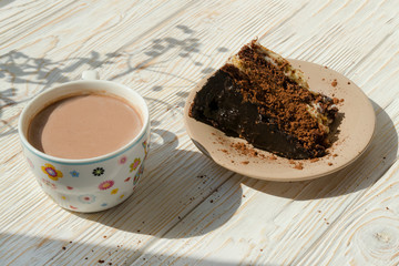 Slice of chocolate cake and cup of hot drink cacao on wooden background with shadow spot