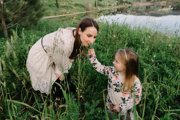 Mother with baby daughter smelling flowers, happy harmonious family outdoors, laughing and playing in the spring on the nature, in the mountains