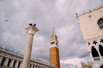 Fototapeta na wymiar A huge bell tower made of red brick in Piazza San Marco - Campanile of St. Mark's Cathedral in Venice, Italy. Against the background of a cloudy, evening, October sunset sky.