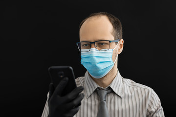 Man in a surgical mask and a tie is making video call. Black background.