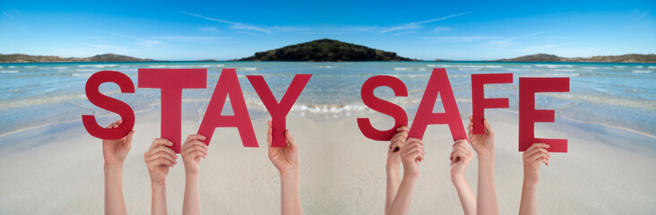 People Hands Holding Colorful English Word Stay Safe. Ocean And Beach As Background