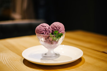 Two balls of delicious lavender purple ice cream with mint leaves in a glass bowl on saucer on the table