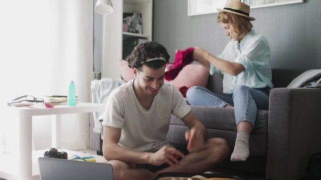 Girl in a hat on the couch and a guy with a laptop sorting things out on a trip
