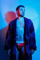 A man in a bathrobe and underwear. Studio lighting red and blue on a male body. Outrageous guy model