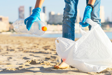 Clean beach from plastic. Hand picking up plastic bottle trash from the beach and putting into...