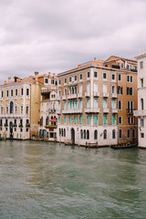 Fototapeta na wymiar A gondola with tourists is sailing along the Grand Canal amid the facades of Venetian houses standing on the water in Venice, Italy.