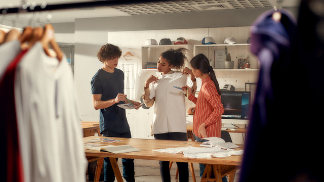 When quality really matters. Creative people trying on stickers with text, while discussing logo and design of T-shirt. Young man and women working at custom T-shirt, clothing printing company