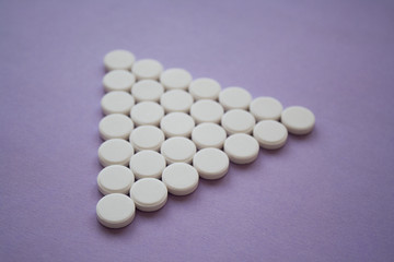 Round medicinal pills in the shape of a large triangle on a dark pink background, isolated.