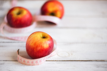 Healthy food and fitness concept. Delicious apple with measuring tape on wood background