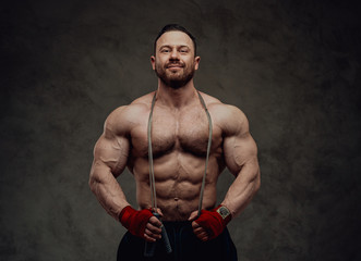 Fototapeta na wymiar Shirtless male bodybuilder showing his muscles while holding a skipping rope in a studio