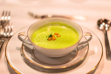 Green peas creamy soup in a white bowl decorated with gildings as appetizer of a restaurant of French cuisine.