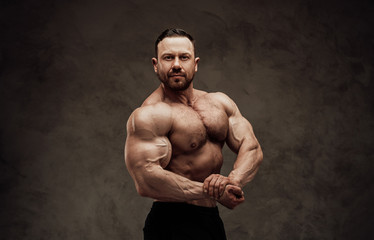Fototapeta na wymiar Sportive adult male wearing shorts showing his biceps muscles in a dark studio
