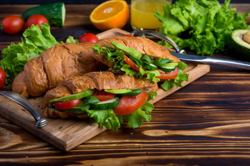 vegan croissants, sandwiches on a wooden table, croissants with avocado, tomatoes and greens, concept of vegan cuisine.

