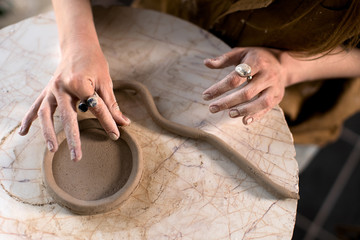 Crop potter making coil vessel on marble table in workshop - obrazy, fototapety, plakaty