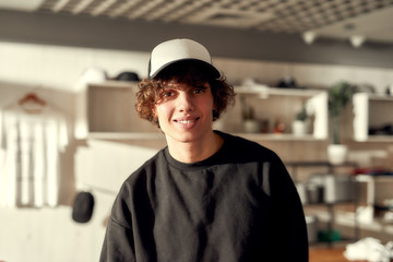 Streetwear. Stylish guy smiling at camera while posing in custom apparel, black baseball cap and...