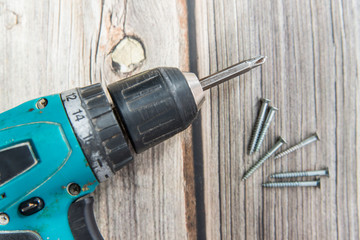 Old screwdriver and screws laying on the wooden background. Flat lay view of the electric screw driver
