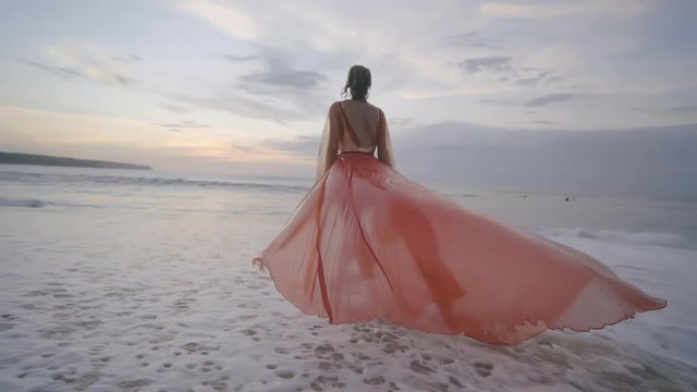 Back view of beautiful fashionable woman on empty beach by sea