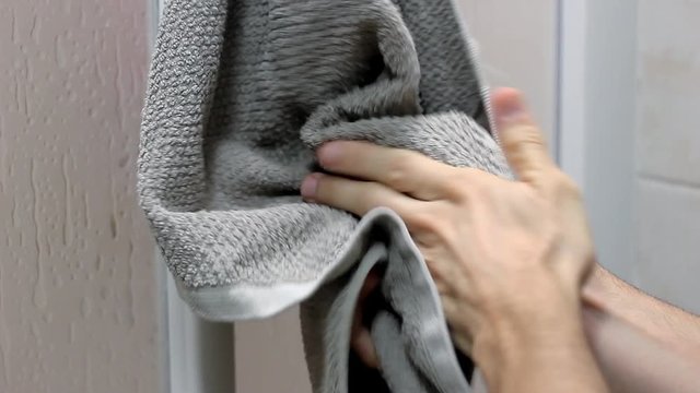 Closeup on hands of man drying off on hanging grey towel in bathroom. Hygiene, skin care, cleaning routine concepts