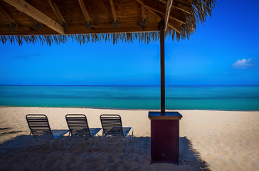 Sun Lounger chairs under a hut on an empty Seven Mile Beach in the Caribbean during confinement, Grand Cayman, Cayman Islands