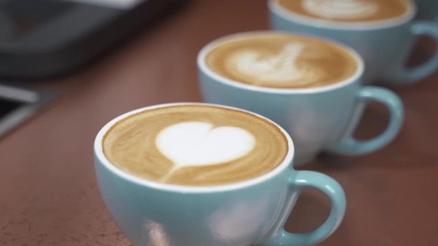 tazas de café con leche azul con diferentes dibujos de latte art hecho por barista en cafetería